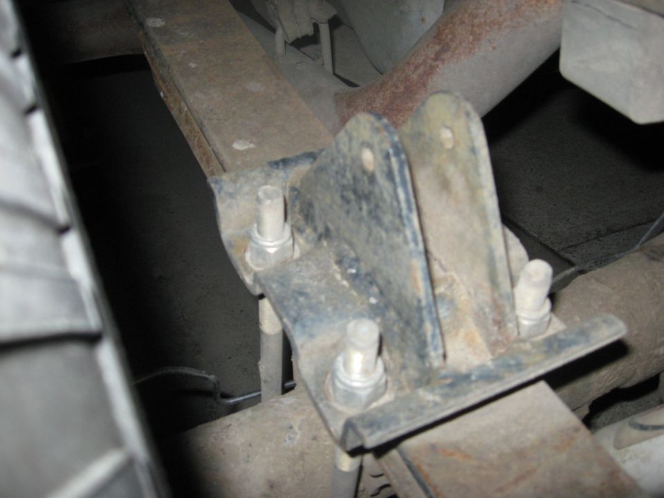 Rusty u-bolt spring plate and nuts clamping a leaf spring to an axle tube, viewed from under the truck