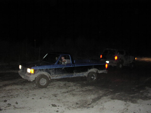 Blue pickup truck and another truck driving off-road at night