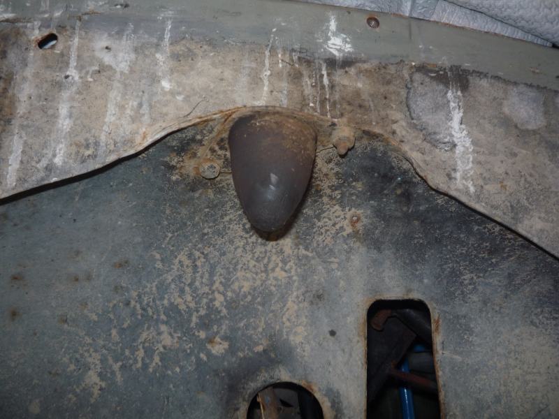 Undercarriage of a vehicle showing a dark, conical component and rusted metal