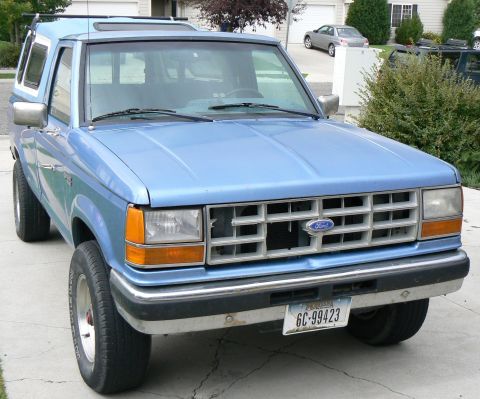 2006 Ford E350 - This blue pickup truck with a camper shell is seen from the front 3/4 angle.