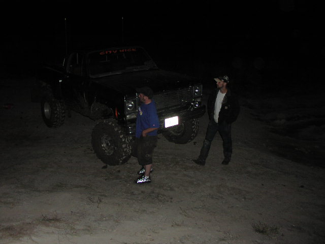 Black pickup truck with oversized tires and two men standing nearby at night