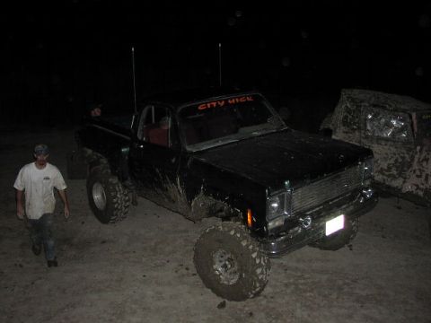 1981 Ford Bronco - A black pickup truck with a "CITY HICK" banner on the windshield is seen off-road at night, with another vehicle in the background.