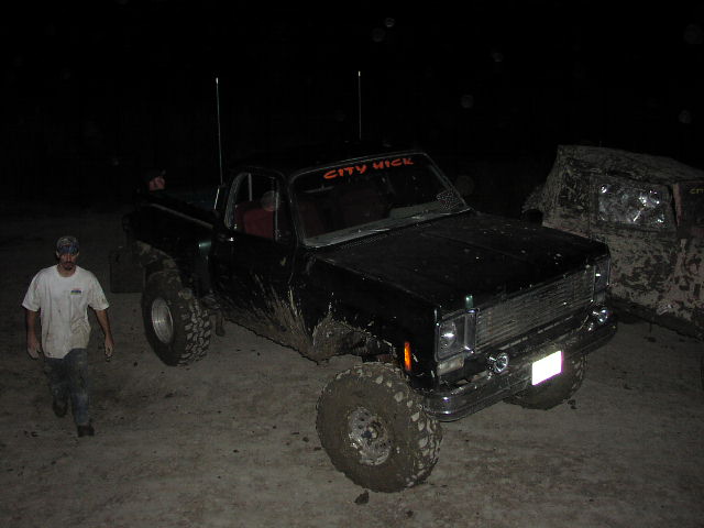 Black pickup truck with lifted suspension and off-road tires, "CITY HICK" windshield banner