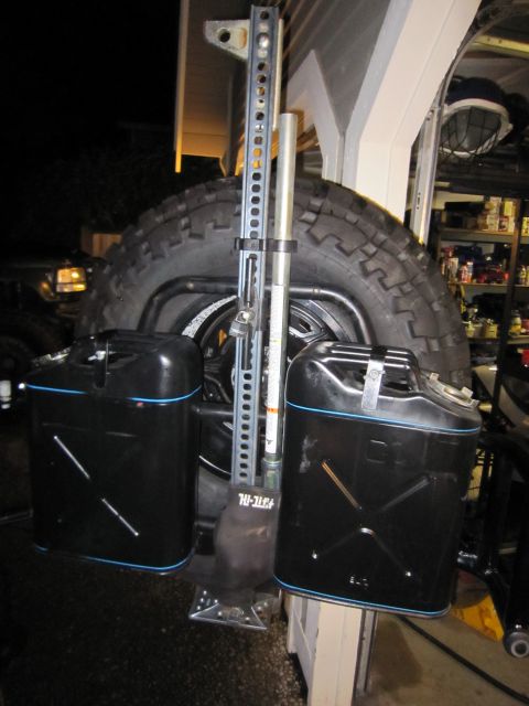 2008 Jeep Wrangler - A Hi-Lift jack and two black jerry cans are mounted to the spare tire carrier of an off-road vehicle.