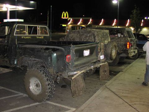 1981 Ford Bronco - Several off-road vehicles, covered in mud, are parked in a lot at night with a McDonald's in the background.