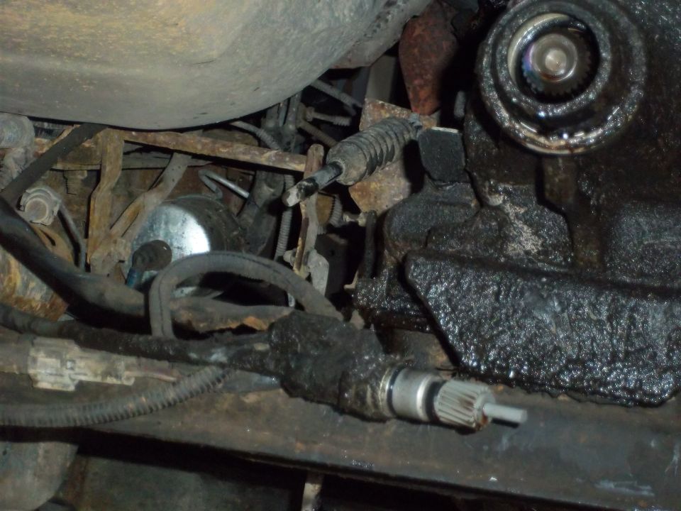 Underside of a vehicle showing a greasy steering component and exhaust pipe
