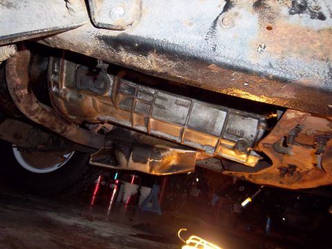 1989 Ford F-150 - The transmission and undercarriage of a vehicle are visible, supported by jack stands in a garage setting.