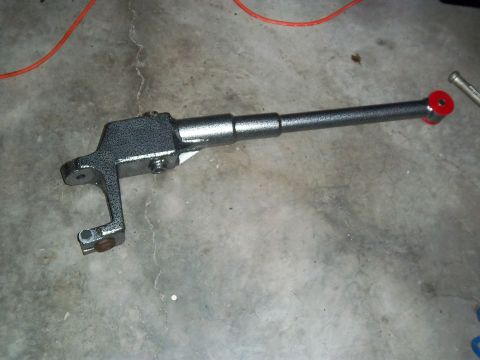 1989 Ford F-150 - A single gray suspension part with a red bushing lies on a concrete surface.