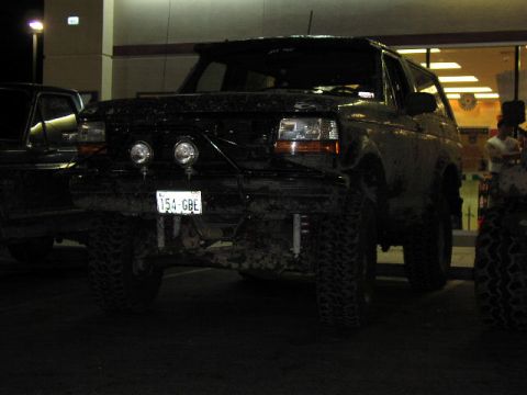 1981 Ford Bronco - This muddy black Ford Bronco, seen from the front, features off-road tires and auxiliary lights.