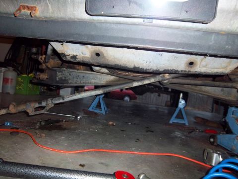 1989 Ford F-150 - The underside of a vehicle is raised on jack stands, showing suspension components and a garage floor with tools.