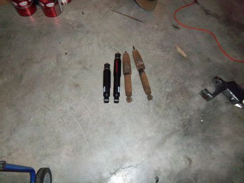 1989 Ford F-150 - Two new black shock absorbers and two old rusty ones lie on a concrete floor.