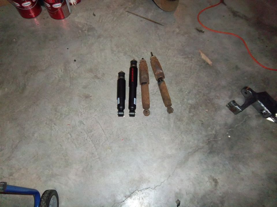 Four shock absorbers on a concrete floor; two are black and two are rusty brown