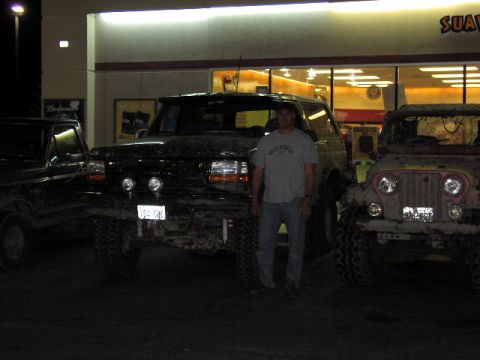 1981 Ford Bronco - Three muddy off-road vehicles and a man stand in front of a convenience store at night.