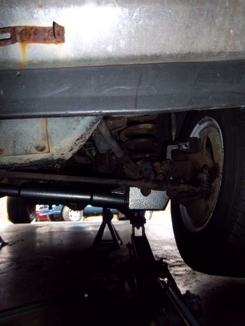 1989 Ford F-150 - The underside of a vehicle is shown, supported by jack stands, with other vehicles visible in the distance.