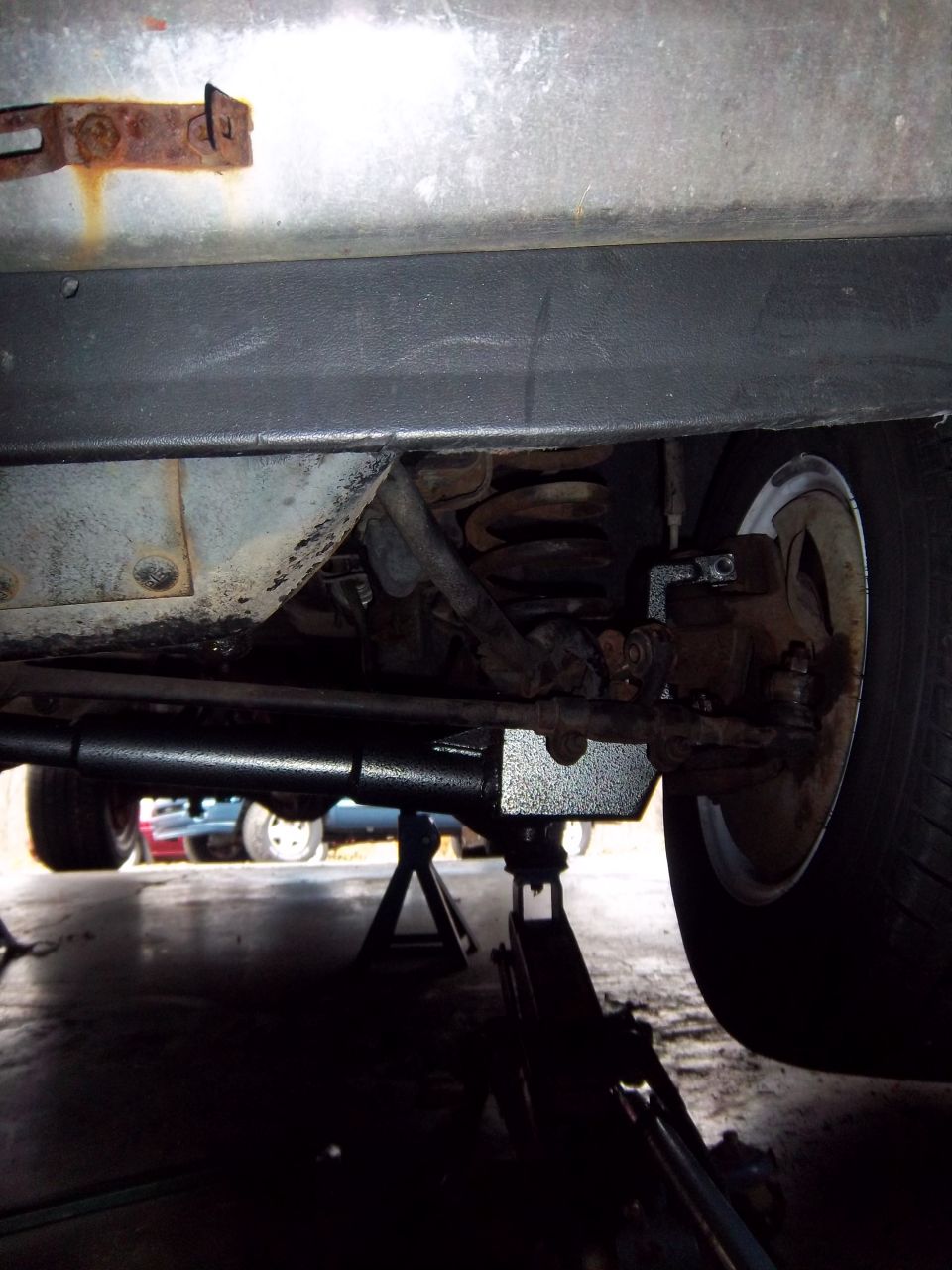 Undercarriage view showing suspension and jack stands with other vehicles in background