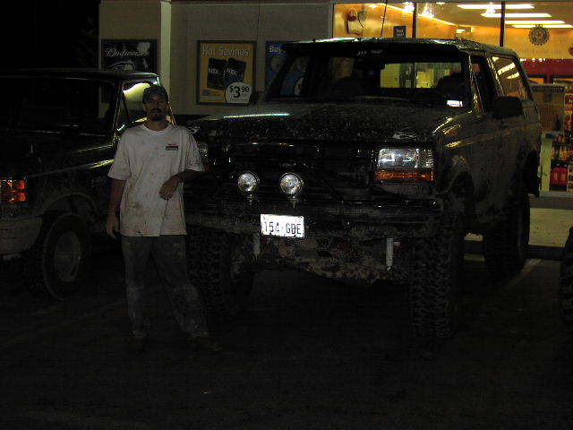 Man stands by a muddy black SUV, another vehicle to the left