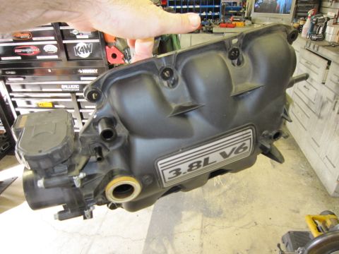 2008 Jeep Wrangler - A black engine intake manifold with a "3.8L V6" label is held by a hand.