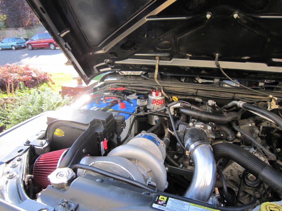 Engine bay with supercharger, battery, and air intake. Hood is open