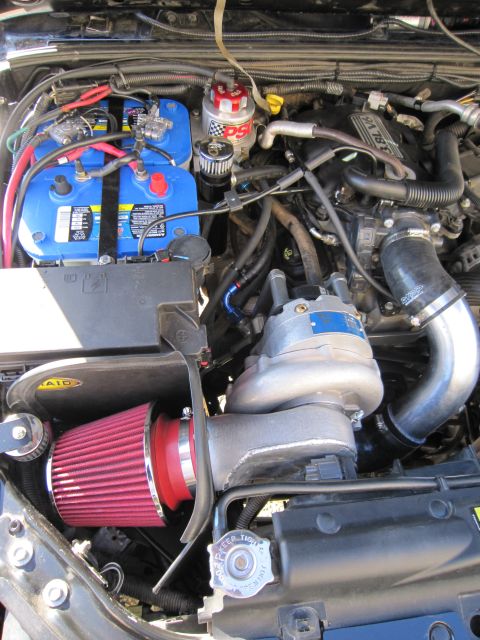 2008 Jeep Wrangler - Engine bay with aftermarket turbocharger, dual batteries, and red air filter.