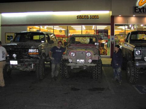 1981 Ford Bronco - Three off-road vehicles are parked in front of a store with a "Suava Java" sign.