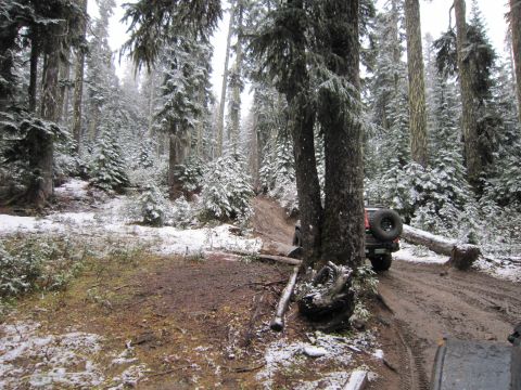 2008 Jeep Wrangler - A Jeep navigates a muddy, snow-dusted forest trail, with another vehicle's front end visible in the foreground.