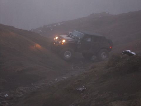 2008 Jeep Wrangler - A black Jeep Wrangler Rubicon navigates a steep, muddy incline in foggy conditions.