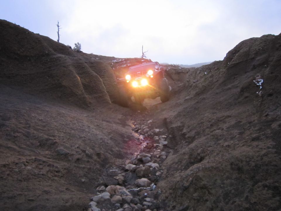 Jeep Wrangler driving down a rocky ravine with headlights on