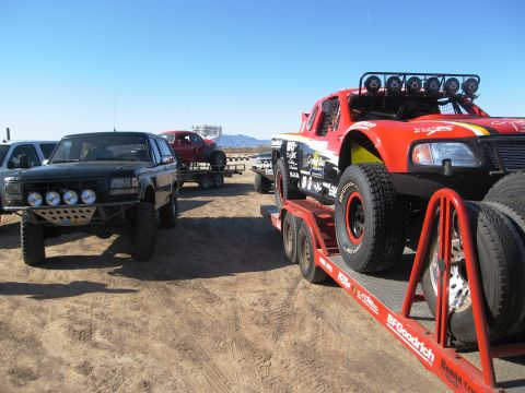 1986 Ford Bronco - A black SUV, possibly a 1992 Ford Bronco, sits in a desert landscape next to a trailer carrying a red off-road truck.