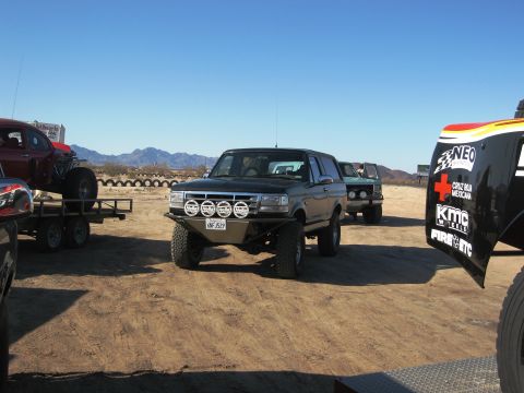 1986 Ford Bronco - Off-road vehicles gathered in a desert landscape under a clear blue sky.