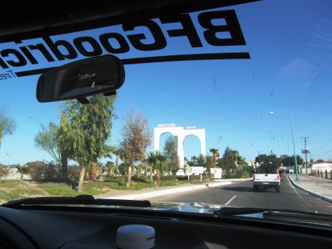 1986 Ford Bronco - A white pickup truck drives down a road with a large archway in the background.