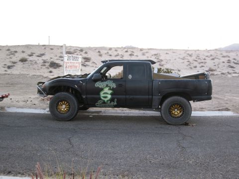 1986 Ford Bronco - A modified black pickup truck sits on the side of a road in a desert-like environment.