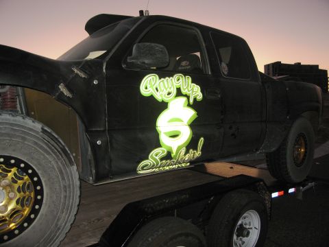 1986 Ford Bronco - Customized black pickup truck with large graphics is loaded onto a trailer.