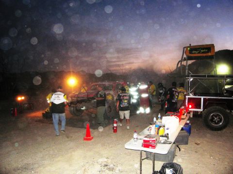 1986 Ford Bronco - A group of people gather around a modified off-road vehicle at dusk, with a trailer and equipment nearby.