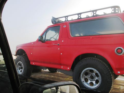 1986 Ford Bronco - This red SUV, likely a 1992 Ford Bronco, is equipped with a roof rack and off-road tires.