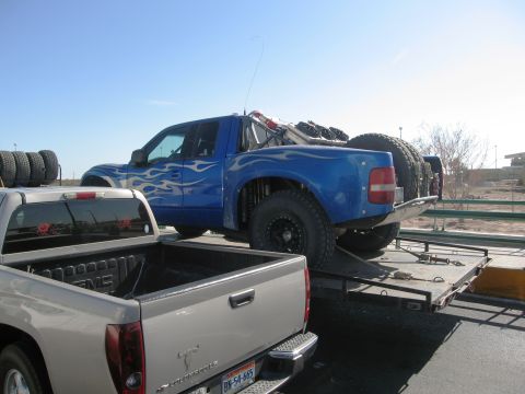 1986 Ford Bronco - A blue off-road truck with flame decals is being transported on a trailer.