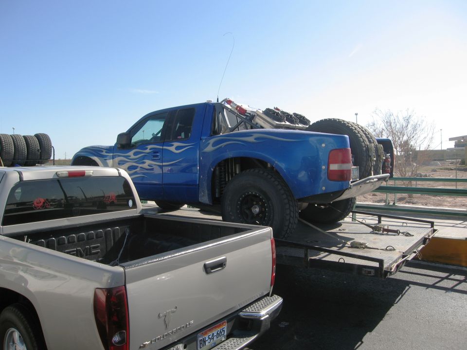 Blue off-road truck with flame decals on a trailer, spare tires visible