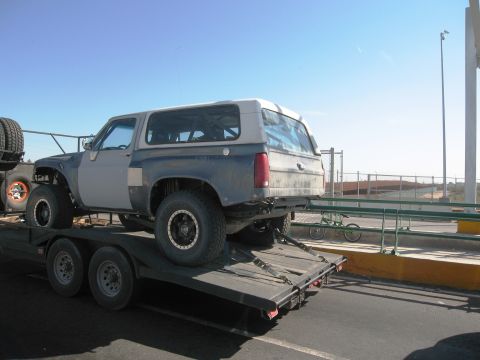 1986 Ford Bronco - Modified 1986 Ford Bronco being transported on a trailer under a clear sky.