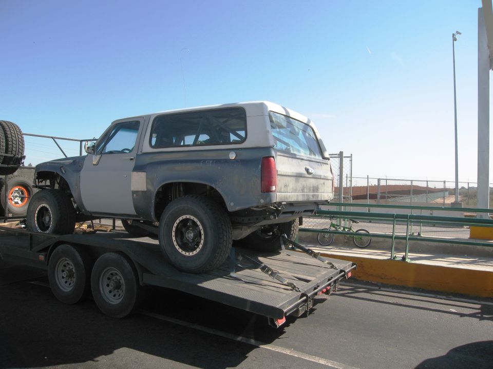 1986 Ford Bronco on a flatbed trailer, modified with large tires and fender flares