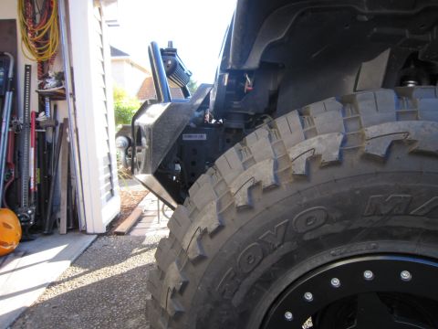 2008 Jeep Wrangler - Low front-corner shot of a black Jeep in a garage doorway with the fender flare removed, showing a Toyo M/T mud-terrain tire on a black bea…