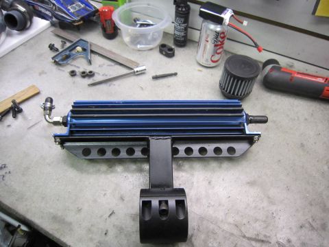 2008 Jeep Wrangler - A blue oil cooler assembly with a black mounting bracket is shown on a workbench with tools and other parts.