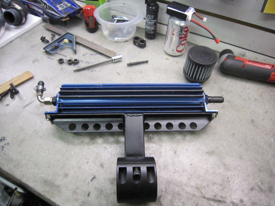 Blue oil cooler with black mounting bracket and fittings on a workbench