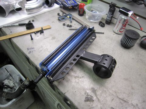 2008 Jeep Wrangler - A close-up view of a custom-made metal bracket with blue fins, resting on a workbench alongside various tools and a can of Diet Coke.
