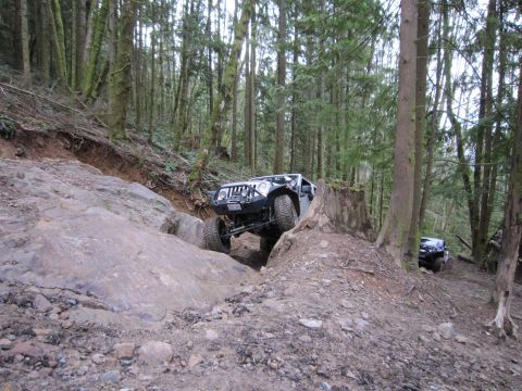 2008 Jeep Wrangler - A white Jeep Wrangler tackles a challenging rocky incline in a forest, with another Jeep visible in the background.