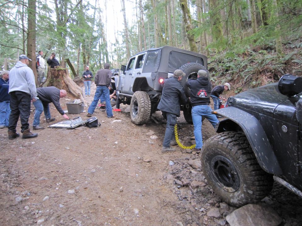Two Jeep Wranglers on a dirt trail in a forest, with people working on one of them