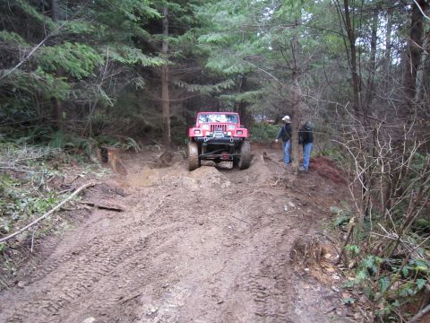 2008 Jeep Wrangler - A red Jeep Wrangler navigates a challenging muddy trail through a dense forest.