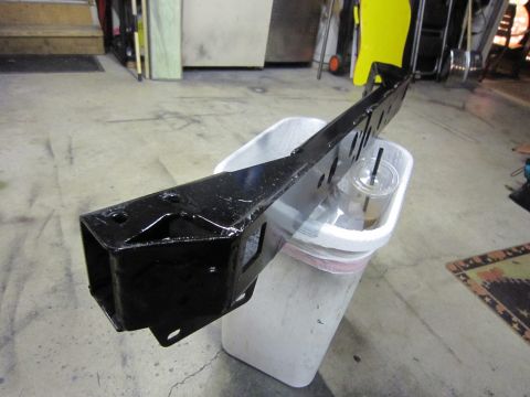 2008 Jeep Wrangler - Black metal suspension component, possibly for a Jeep Wrangler, sits on a bucket in a garage.