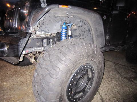 2008 Jeep Wrangler - Close-up view of the front fender and wheel well of a black Jeep Wrangler, highlighting the blue coilover suspension and aggressive off-roa…