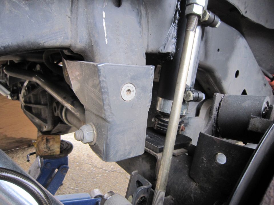 Fabricated bare-metal frame bracket beside track bar and shock on a lifted chassis