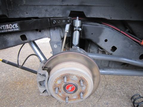 2008 Jeep Wrangler - Wheel-off view of a solid-axle front suspension with the disc rotor and caliper still on the hub, a Superchip-branded hub cover, and a poli…