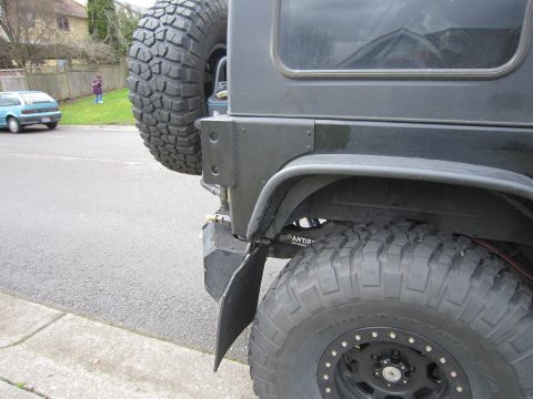 2008 Jeep Wrangler - The rear corner of a black SUV is shown, a spare tire, mud flap, and aftermarket bumper components.